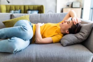 Young woman lying on sofa in extreme discomfort, appearing to experience nausea