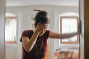 Woman holding her head with both hands appearing disoriented, with blurred motion effect suggesting dizziness or vertigo symptoms.