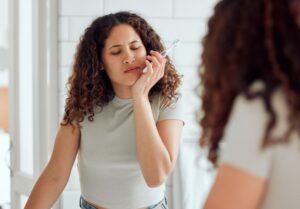 African American woman wincing in pain while brushing her teeth, holding her jaw to indicate dental discomfort or toothache.