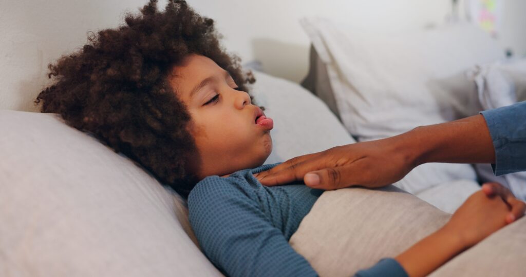 Father comforting sick child lying in bed, hand placed on child's chest as child coughs.