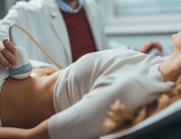 Doctor performing abdominal ultrasound examination on patient, holding transducer probe on patient's stomach.
